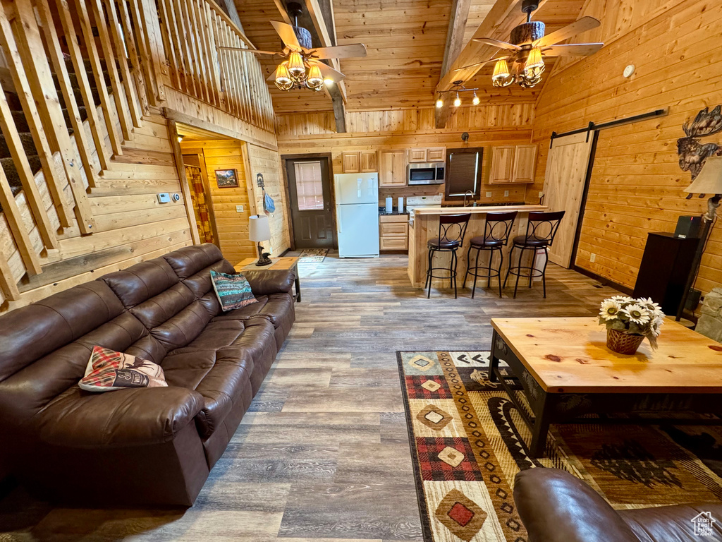 Living area featuring a ceiling fan, wooden walls, a barn door, high vaulted ceiling, and wood finished floors