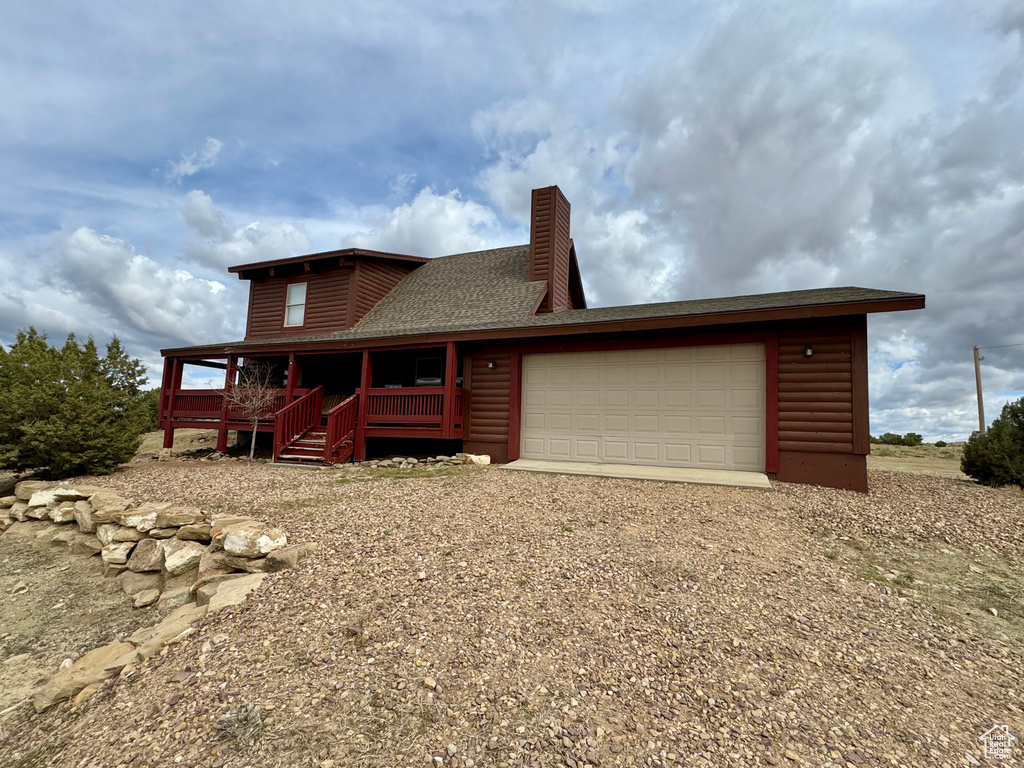 Back of property with faux log siding, a chimney, a garage, driveway, and covered porch