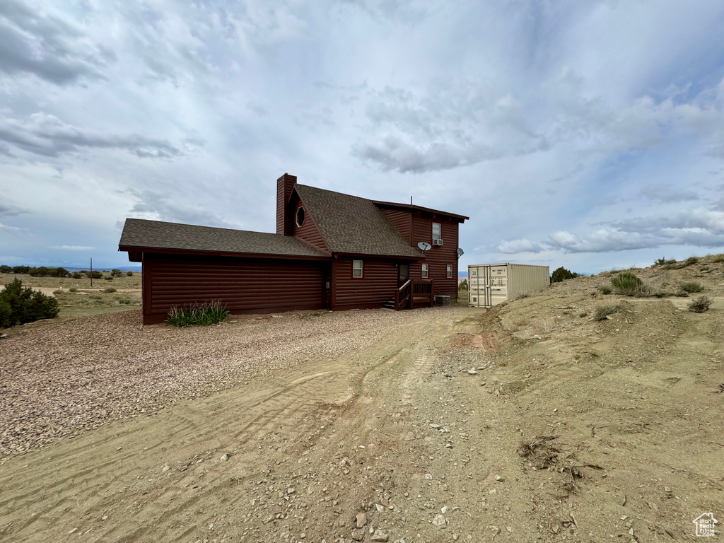 View of side of property featuring dirt driveway, log veneer siding, a chimney, and roof with shingles