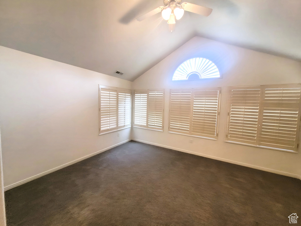 Unfurnished room with lofted ceiling, baseboards, dark colored carpet, visible vents, and ceiling fan