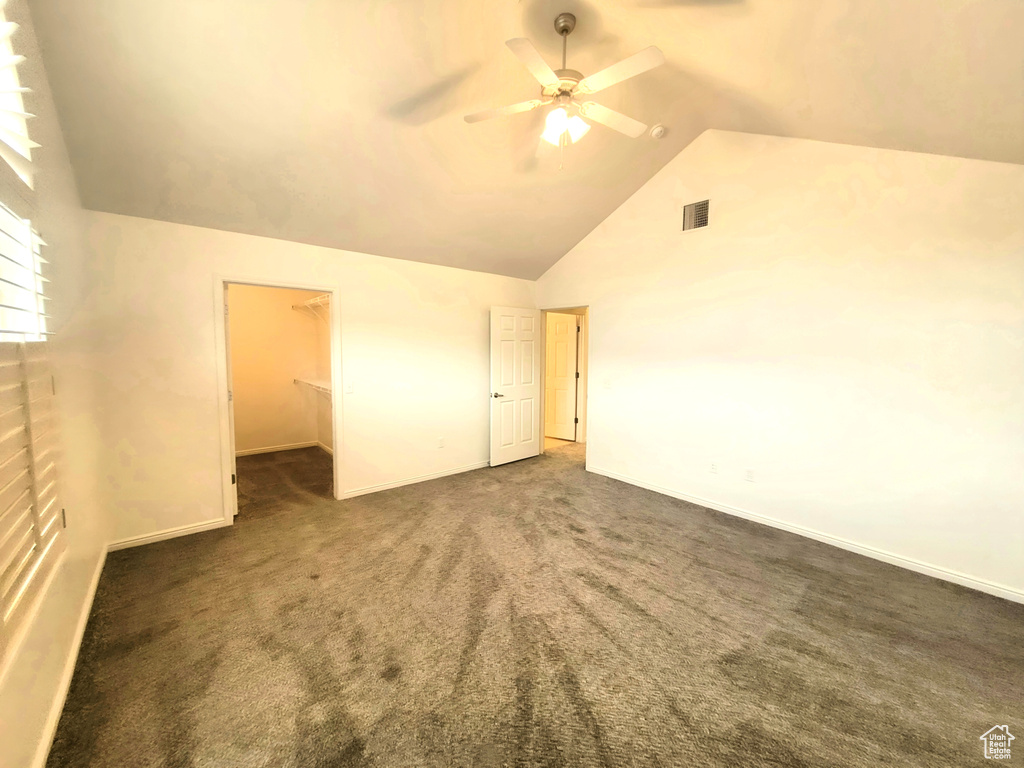 Unfurnished bedroom featuring carpet, visible vents, vaulted ceiling, a walk in closet, and baseboards