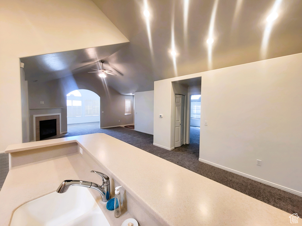 Kitchen with dark carpet, a fireplace with raised hearth, a ceiling fan, baseboards, and lofted ceiling