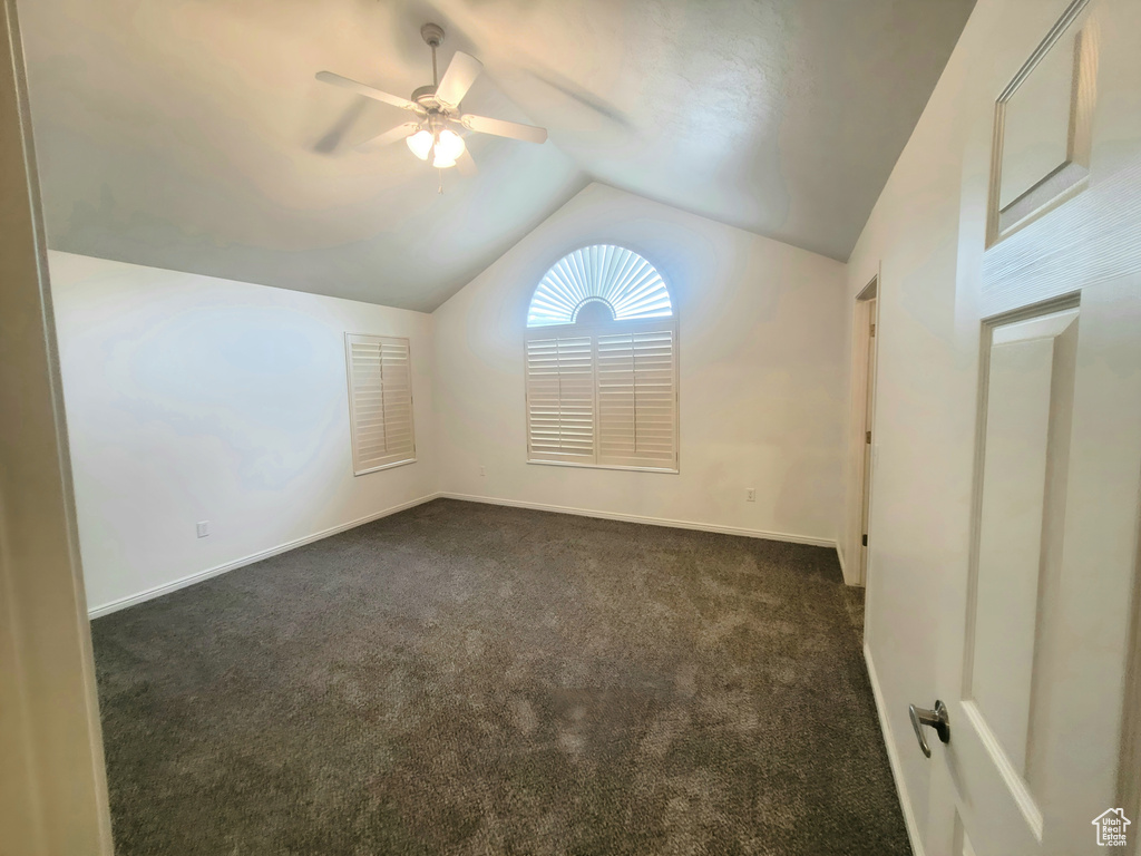 Interior space with baseboards, dark colored carpet, ceiling fan, and vaulted ceiling