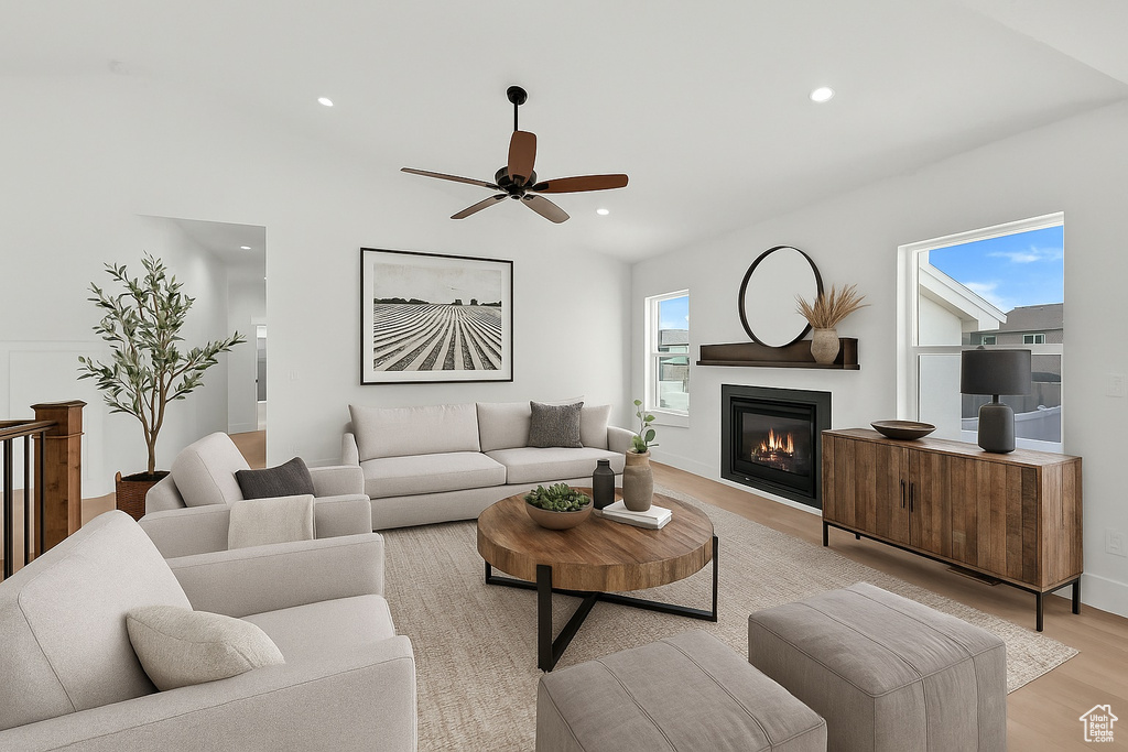 Living room with ceiling fan, light wood-type flooring, lofted ceiling, a glass covered fireplace, and recessed lighting