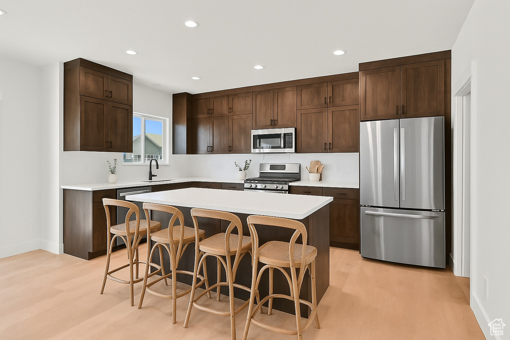 Kitchen with stainless steel appliances, light wood-style floors, dark brown cabinetry, a kitchen bar, and recessed lighting
