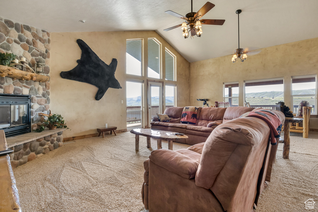 Living room featuring high vaulted ceiling, carpet, ceiling fan, a stone fireplace, and baseboards