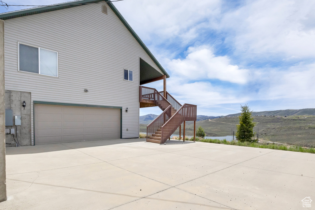 View of side of property with an attached garage, a mountain view, concrete driveway, and stairway