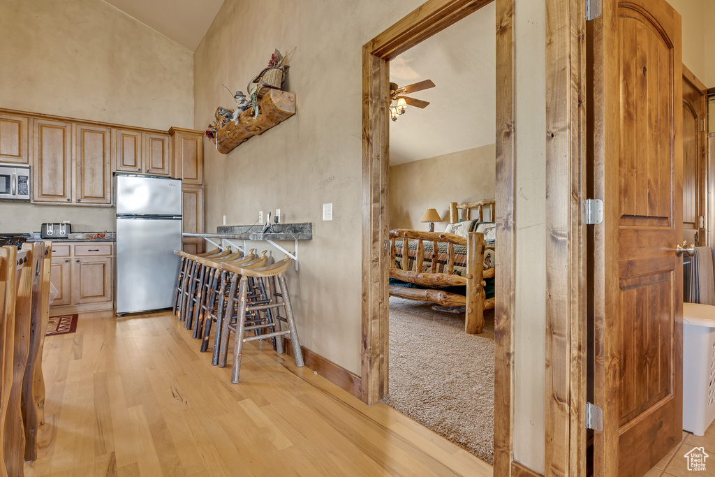 Kitchen with stainless steel appliances, light wood finished floors, high vaulted ceiling, dark countertops, and ceiling fan
