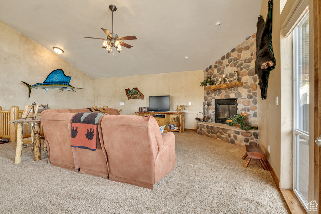 Carpeted living area featuring a ceiling fan, vaulted ceiling, and a stone fireplace