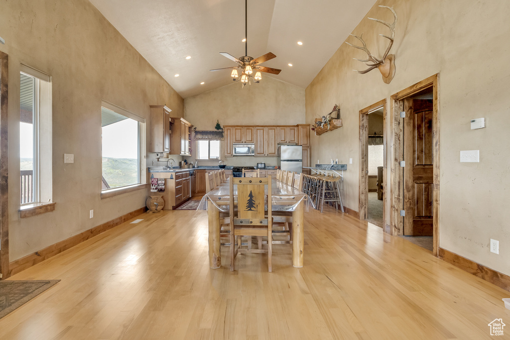 Dining space with a ceiling fan, light wood finished floors, high vaulted ceiling, and baseboards