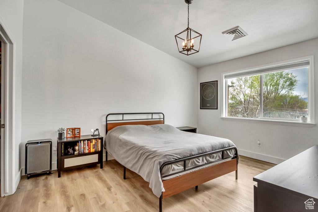 Bedroom with a chandelier, light wood-type flooring, baseboards, and vaulted ceiling
