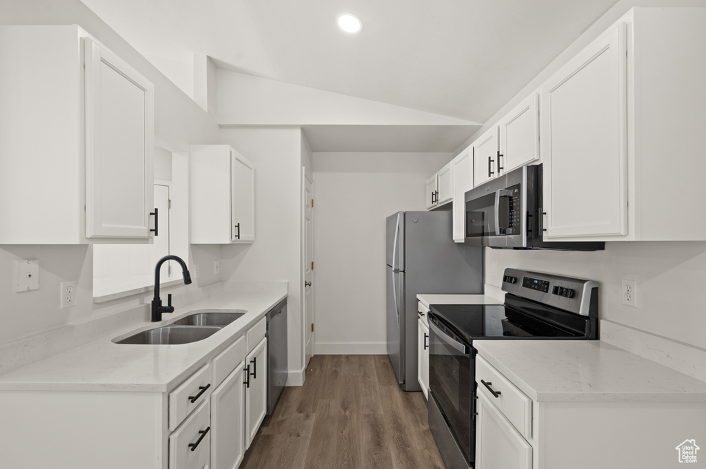 Kitchen with stainless steel appliances, a sink, vaulted ceiling, white cabinetry, and wood finished floors