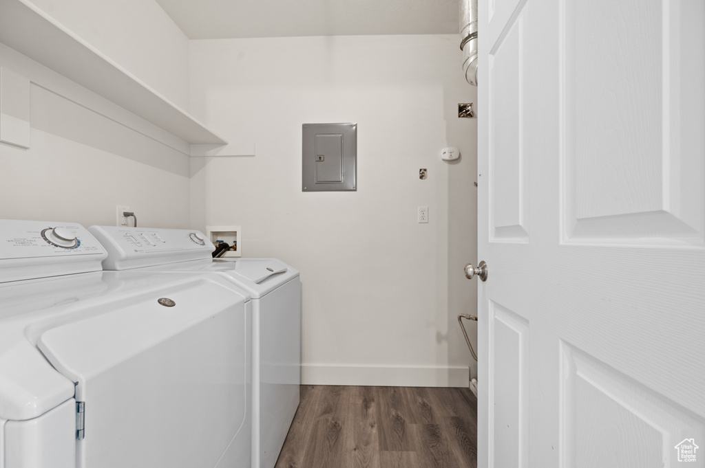 Clothes washing area featuring electric panel, washer and dryer, baseboards, and dark wood-type flooring