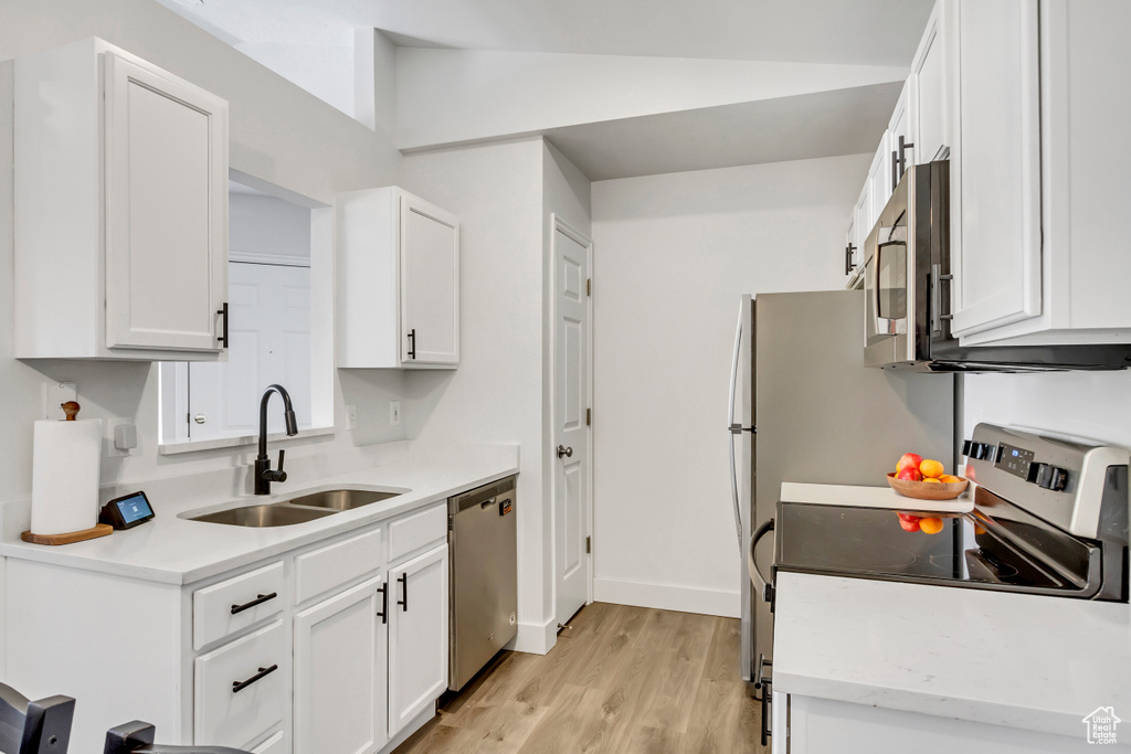 Kitchen featuring stainless steel appliances, a sink, light wood-style flooring, light countertops, and white cabinetry