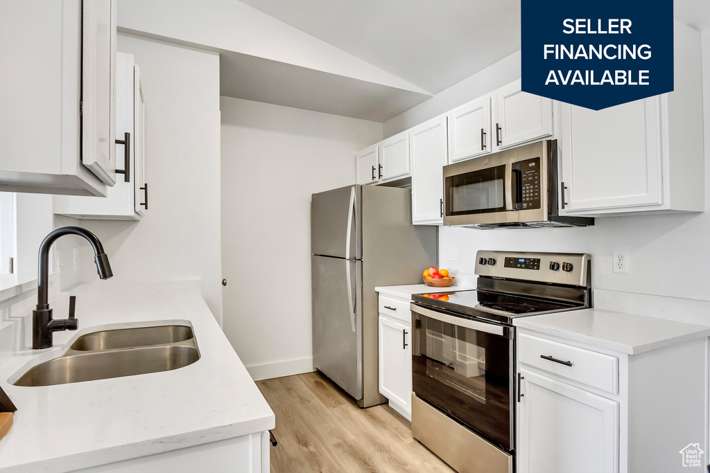 Kitchen featuring stainless steel appliances, a sink, vaulted ceiling, light wood-type flooring, and white cabinets