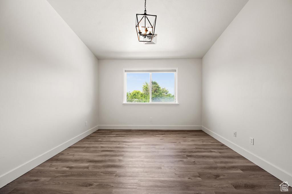 Empty room featuring a chandelier, baseboards, and dark wood-style floors