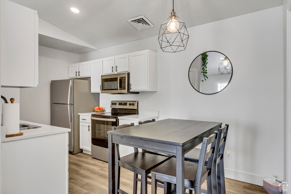 Kitchen featuring stainless steel appliances, white cabinets, light wood-style floors, vaulted ceiling, and light countertops