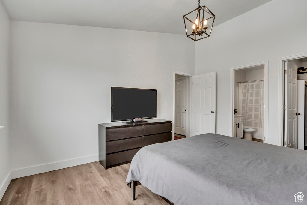 Bedroom featuring baseboards, a chandelier, light wood-type flooring, ensuite bath, and a high ceiling