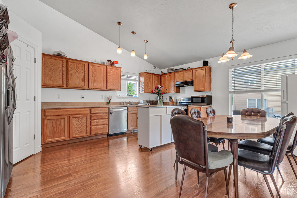 Kitchen with appliances with stainless steel finishes, light wood-style flooring, brown cabinets, hanging light fixtures, and high vaulted ceiling