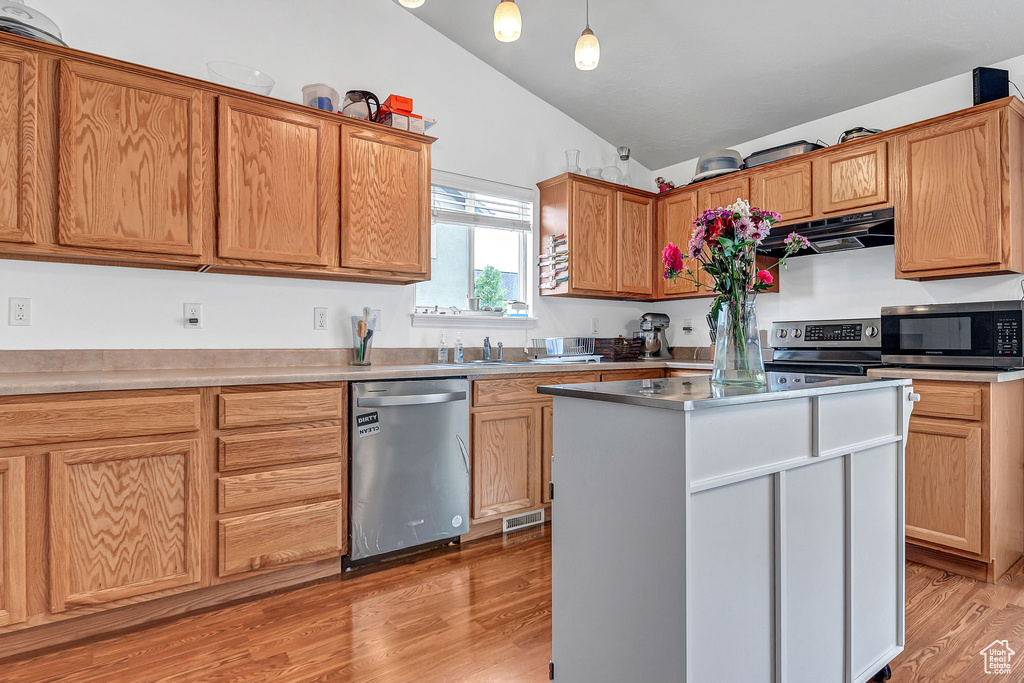 Kitchen with stainless steel appliances, under cabinet range hood, lofted ceiling, light wood-style flooring, and a kitchen island