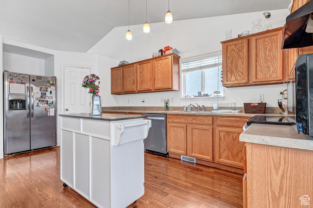 Kitchen featuring appliances with stainless steel finishes, light wood-type flooring, ventilation hood, vaulted ceiling, and a kitchen island