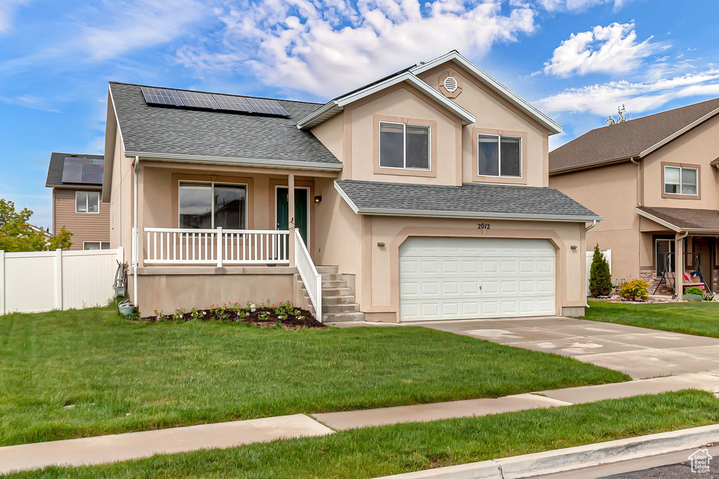 Tri-level home with covered porch, stucco siding, roof mounted solar panels, a shingled roof, and a garage