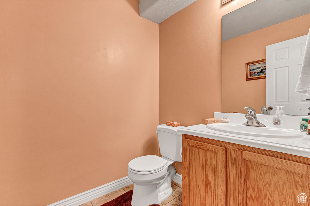 Half bath with toilet, tile patterned flooring, vanity, and baseboards