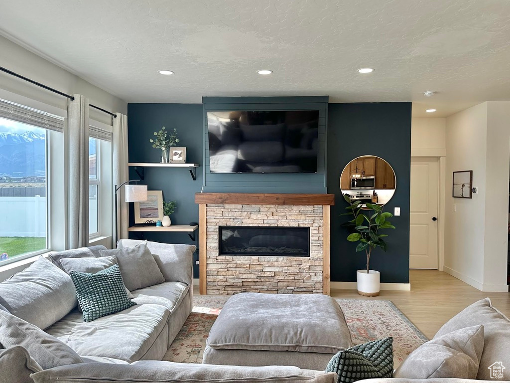 Living room featuring wood finished floors, a stone fireplace, recessed lighting, baseboards, and a textured ceiling