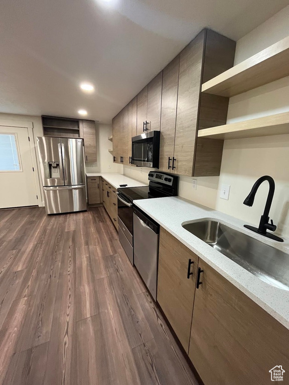 Kitchen with stainless steel appliances, a sink, open shelves, light countertops, and dark wood-style flooring