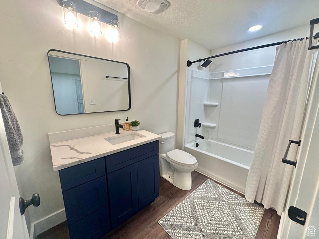 Full bath featuring wood finished floors, toilet, vanity, shower / tub combo with curtain, and a textured ceiling