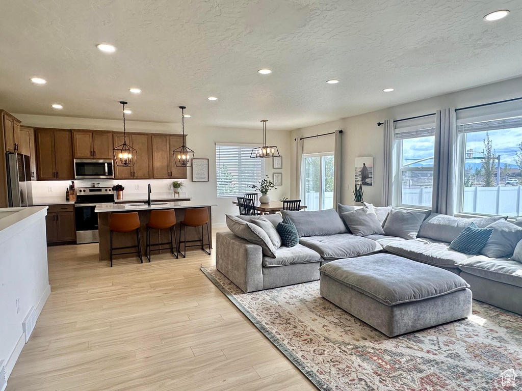 Living room featuring recessed lighting, light wood finished floors, a textured ceiling, a chandelier, and baseboards