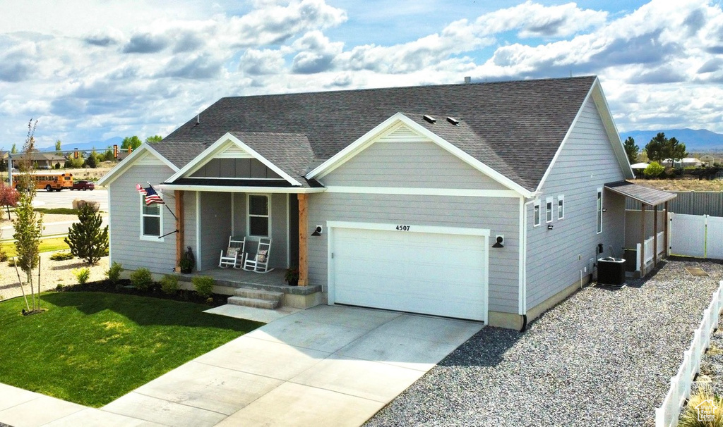 View of front of property with covered porch, a garage, roof with shingles, driveway, and central AC