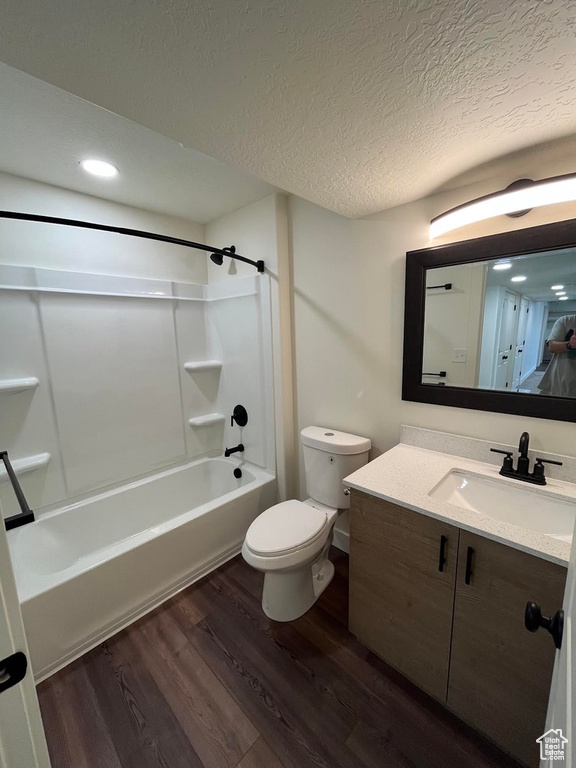 Full bath with wood finished floors, toilet, vanity, a textured ceiling, and bathtub / shower combination