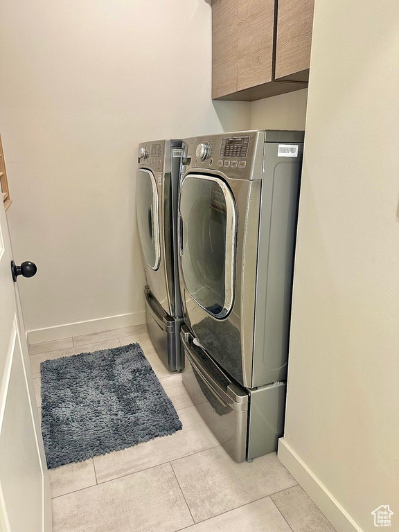 Clothes washing area featuring independent washer and dryer, cabinet space, baseboards, and light tile patterned floors