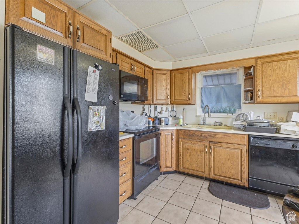 Kitchen featuring black appliances, a sink, light tile patterned floors, light countertops, and brown cabinets