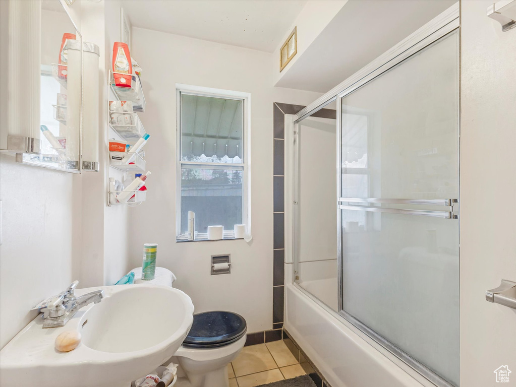 Bathroom featuring a sink, tile patterned floors, toilet, and combined bath / shower with glass door