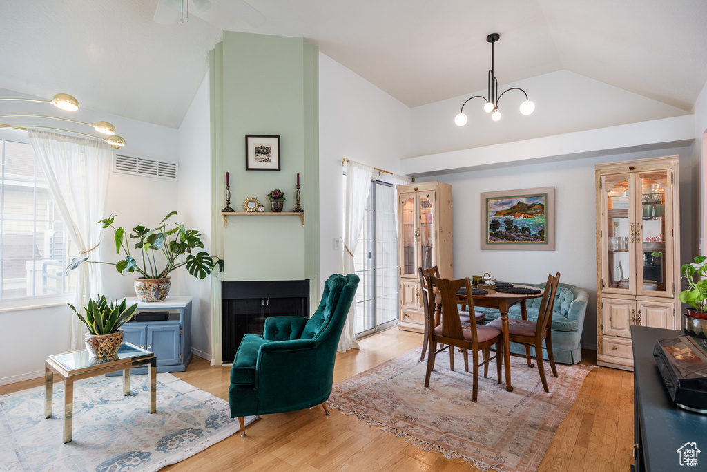 Dining space with lofted ceiling, a chandelier, light wood-style floors, and a fireplace
