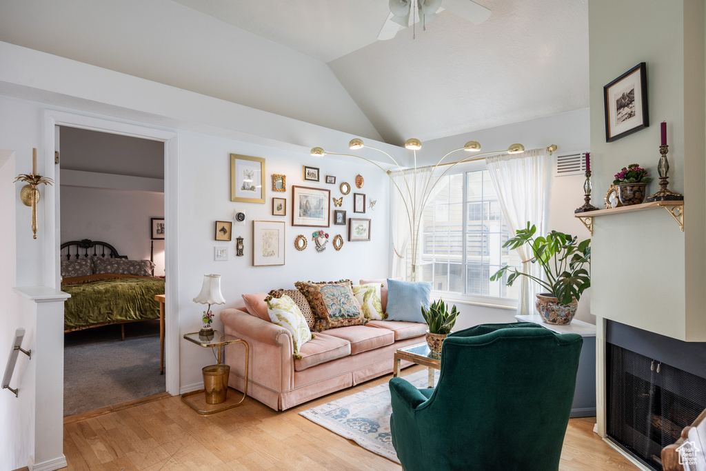 Living room with light wood finished floors, a ceiling fan, lofted ceiling, and a multi sided fireplace