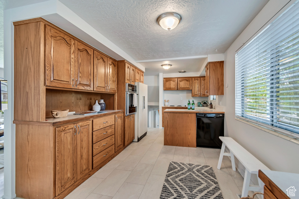 Kitchen featuring dishwasher, oven, brown cabinets, freestanding refrigerator, and a textured ceiling
