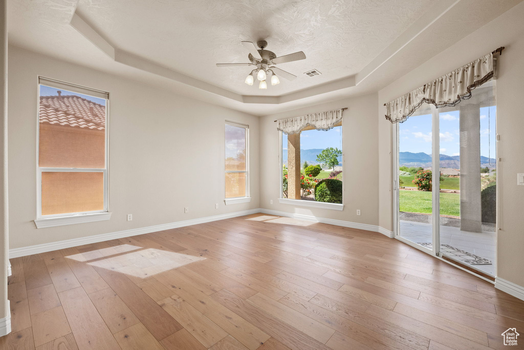 Unfurnished room with a tray ceiling, a ceiling fan, baseboards, and hardwood / wood-style floors
