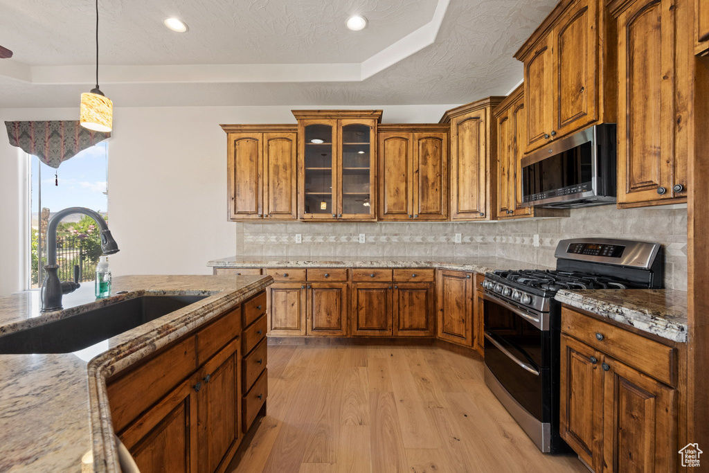 Kitchen with stainless steel appliances, a raised ceiling, a sink, light wood-style floors, and brown cabinets