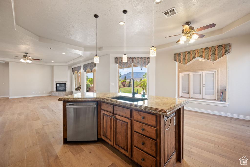Kitchen with a sink, stainless steel dishwasher, ceiling fan, brown cabinetry, and a textured ceiling