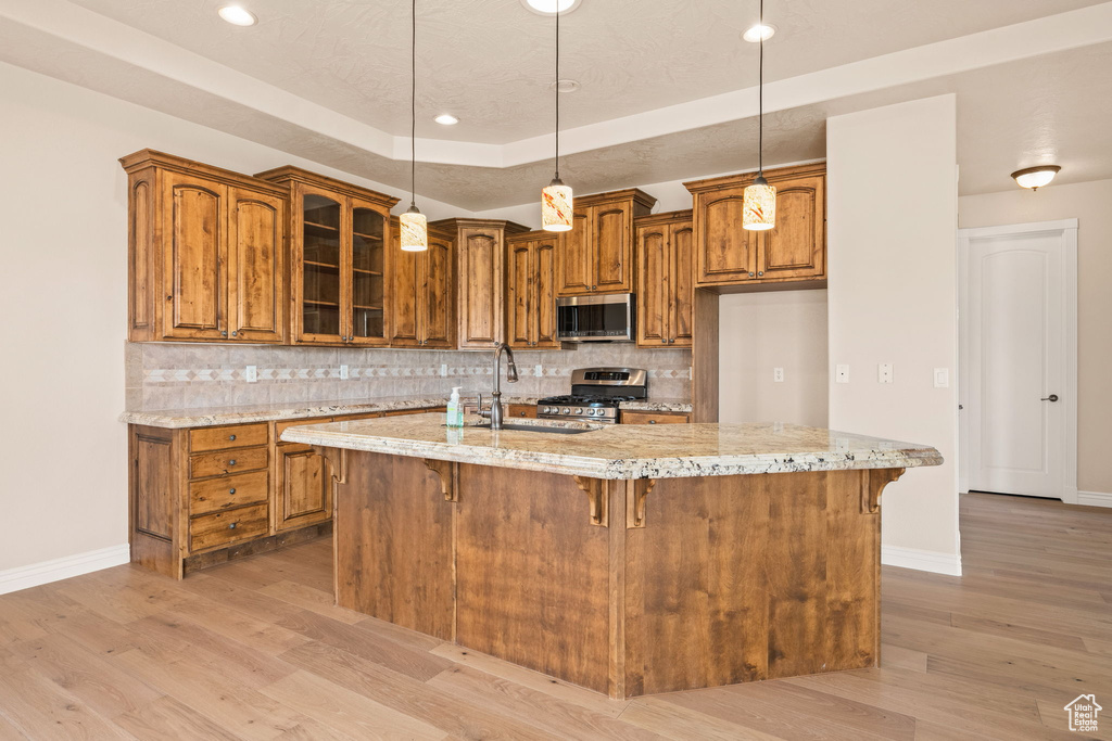 Kitchen with appliances with stainless steel finishes, brown cabinetry, light wood-type flooring, baseboards, and tasteful backsplash