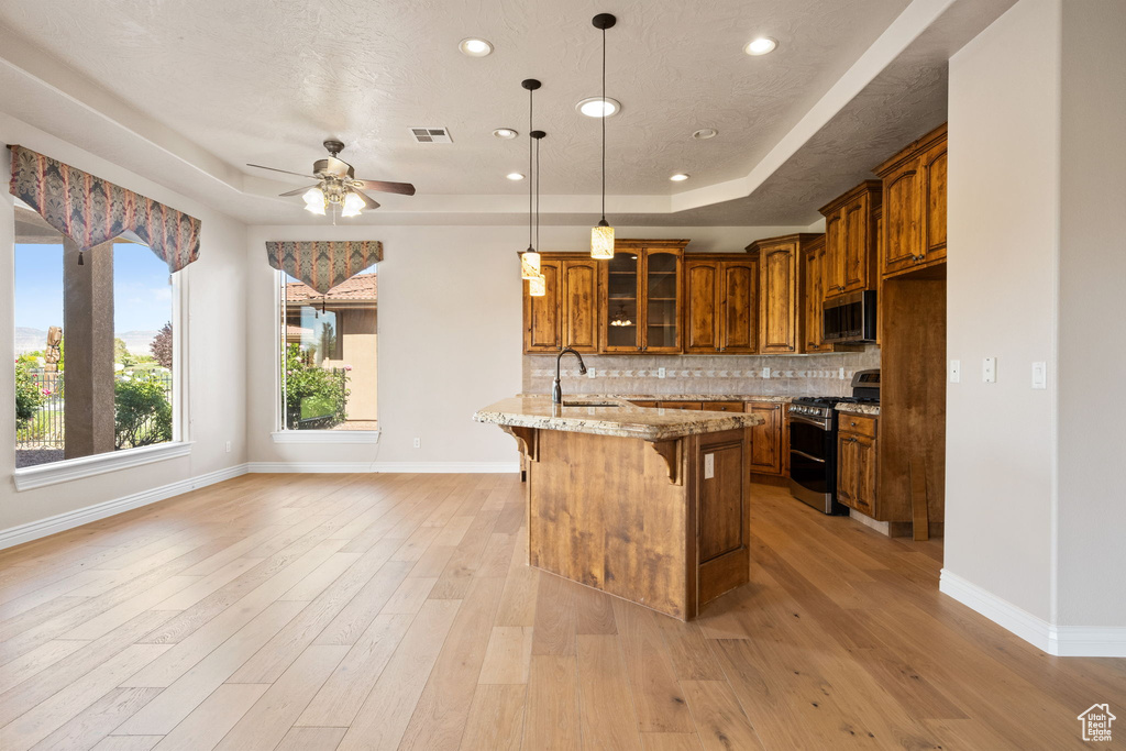 Kitchen featuring stainless steel appliances, a raised ceiling, a kitchen breakfast bar, ceiling fan, and brown cabinets
