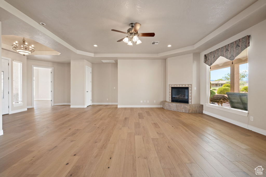 Unfurnished living room featuring a raised ceiling, light wood-style flooring, ceiling fan, a tile fireplace, and recessed lighting