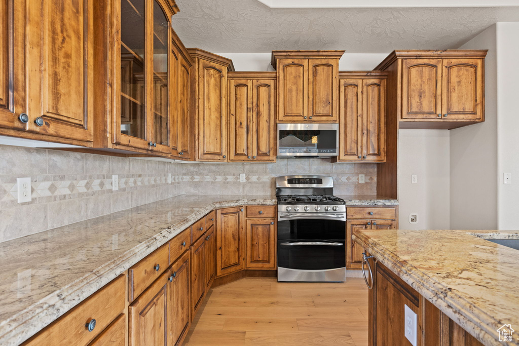Kitchen with appliances with stainless steel finishes, light wood finished floors, light stone countertops, and brown cabinetry