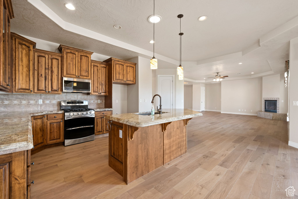 Kitchen with stainless steel appliances, a tray ceiling, brown cabinetry, a sink, and tasteful backsplash