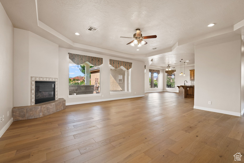 Unfurnished living room with a ceiling fan, a tray ceiling, hardwood / wood-style flooring, baseboards, and recessed lighting