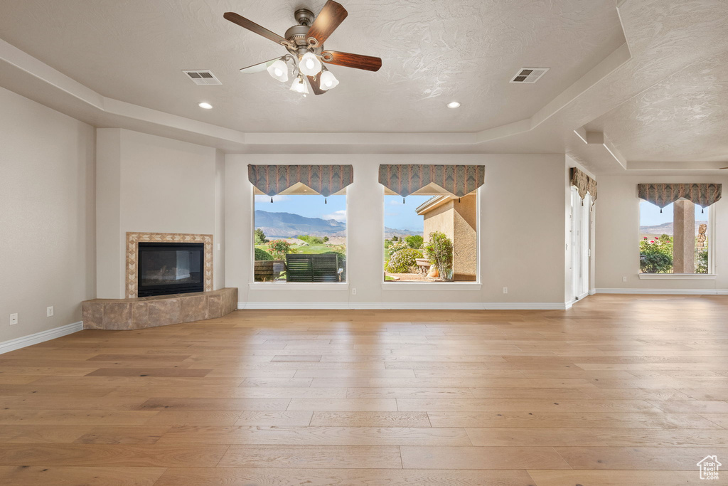 Unfurnished living room featuring a tray ceiling, light wood finished floors, a high end fireplace, baseboards, and a textured ceiling