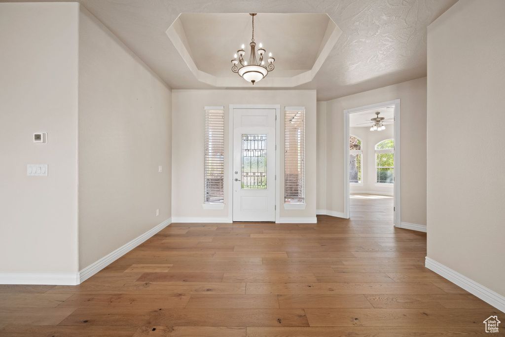 Foyer entrance featuring a raised ceiling, a chandelier, baseboards, and hardwood / wood-style flooring